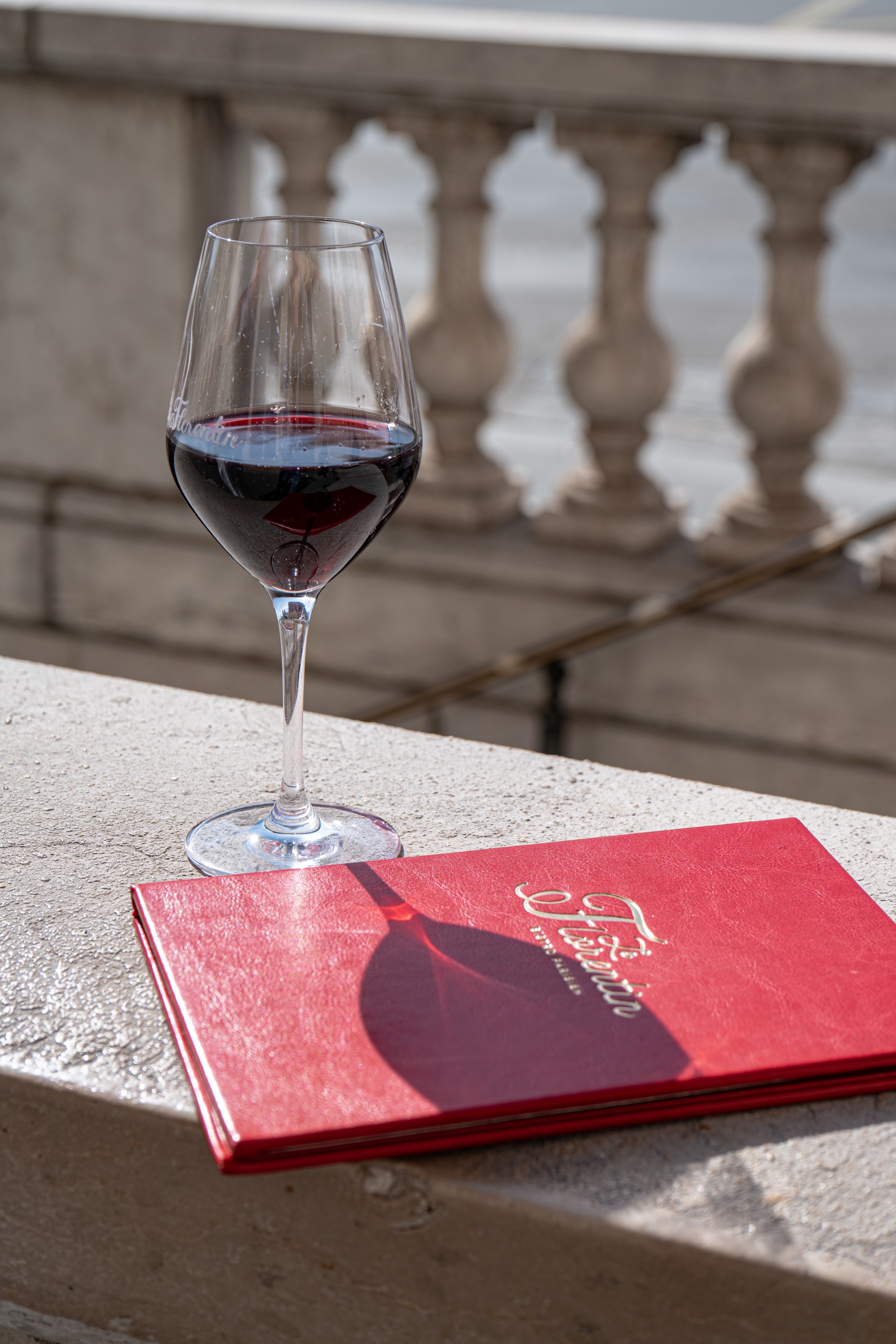 Verre de vin avec carte rouge sur balustrade en pierre, terrasse du Florentin